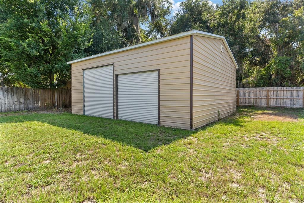 A tan metal storage shed with two roll-up doors sits on a grassy backyard lot — 200 WATERS EDGE DRIVE, LEESBURG, FL