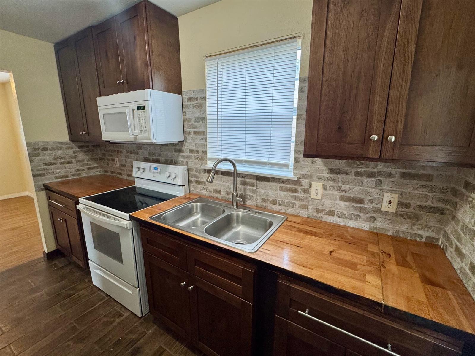 A kitchen features dark wood cabinets, butcher block countertops, a brick backsplash, and white appliances — 714 S Seminole Avenue, FL 33841, FL