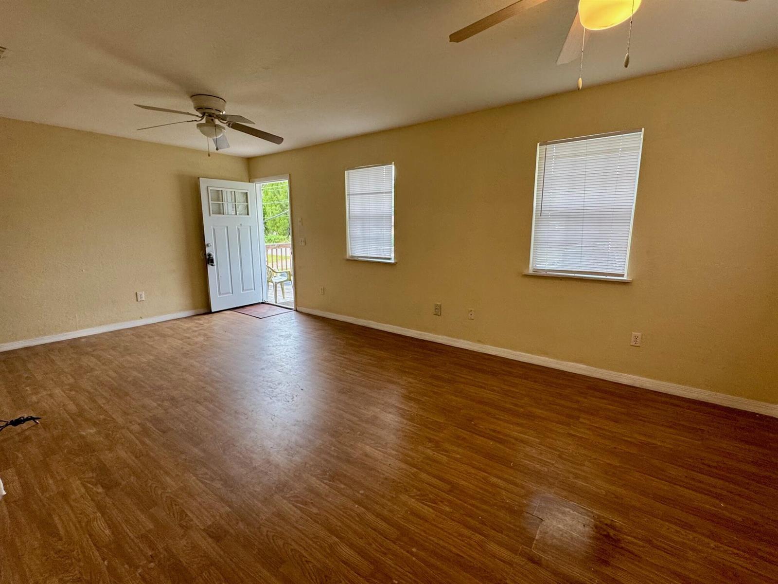 An empty living room features light-colored walls, wood-look flooring, two windows, and a ceiling fan — 714 S Seminole Avenue, FL 33841, FL