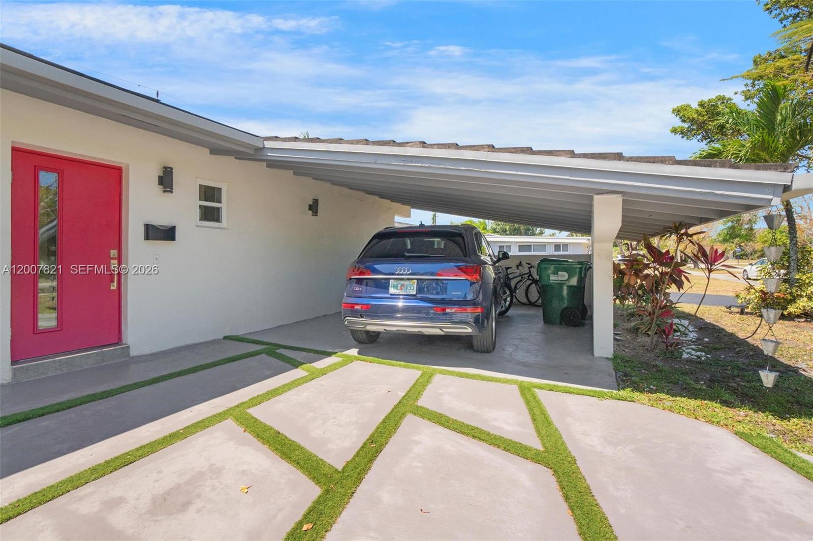 A blue SUV is parked under a carport next to a house with a pink door — PALMETTO BAY, FL