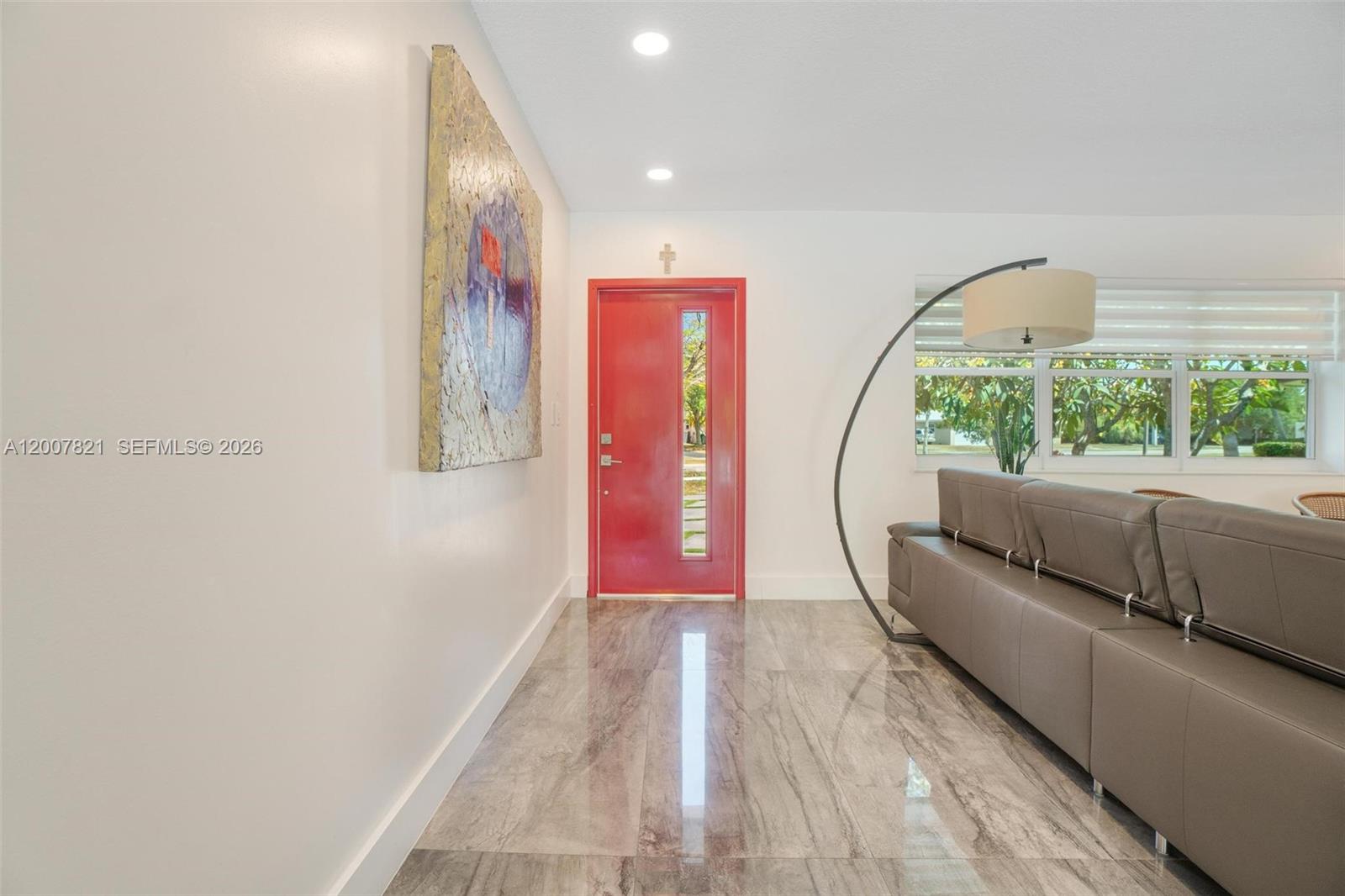 A bright entryway features a red door, marble-look tile flooring, and a large abstract painting — PALMETTO BAY, FL