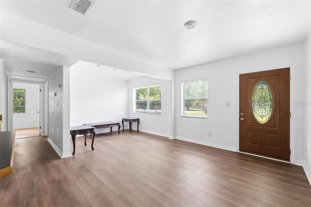 A living room with light wood-look flooring, white walls, and a wooden front door — 27 CROOM ROAD, BROOKSVILLE, FL