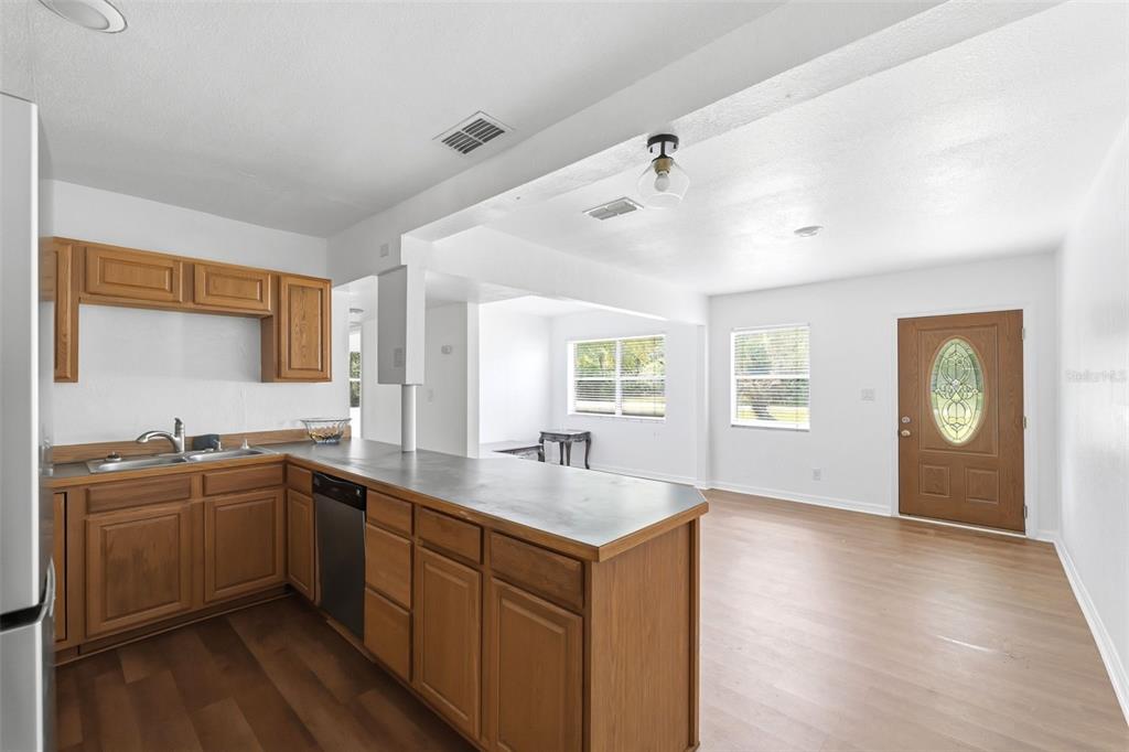 A kitchen with wood cabinets and a breakfast bar opens into a living area — 27 CROOM ROAD, BROOKSVILLE, FL