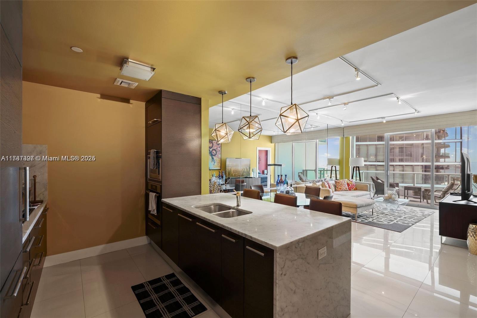 A modern kitchen with a marble island and dark cabinets opens into a living area — 900 Biscayne Blvd # 2410, Miami FL 33132, MIAMI, FL