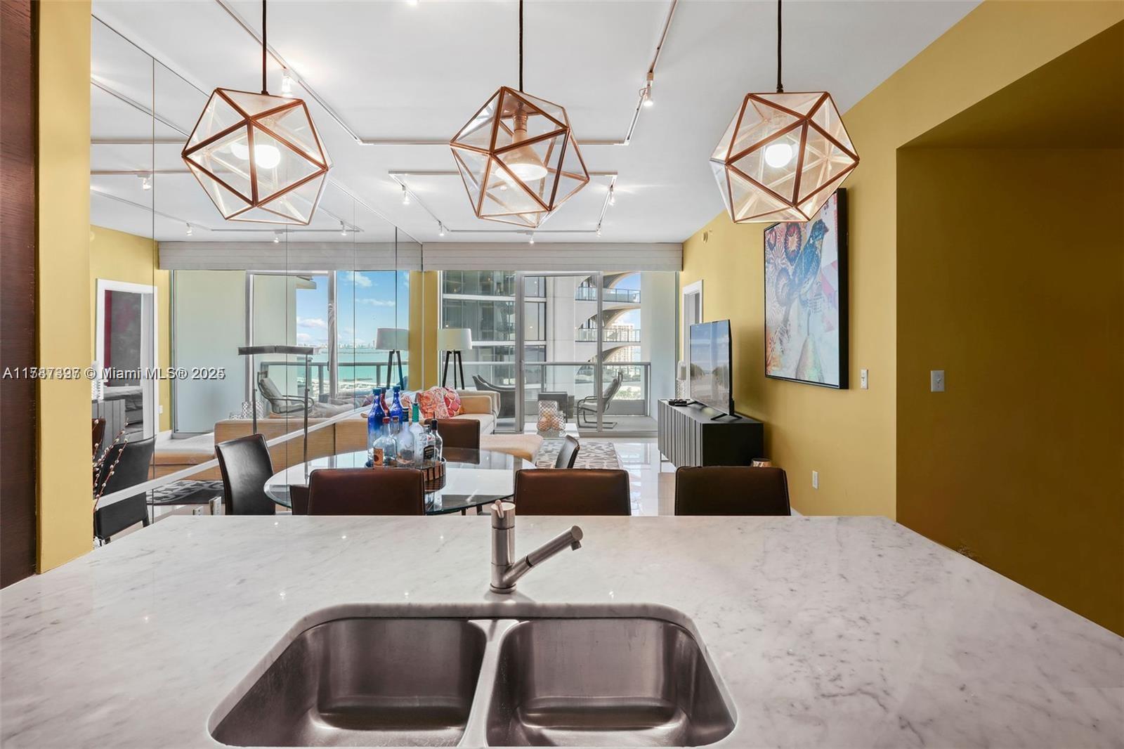 A kitchen island with a double sink overlooks a dining area and a living room — 900 Biscayne Blvd # 2410, Miami FL 33132, MIAMI, FL