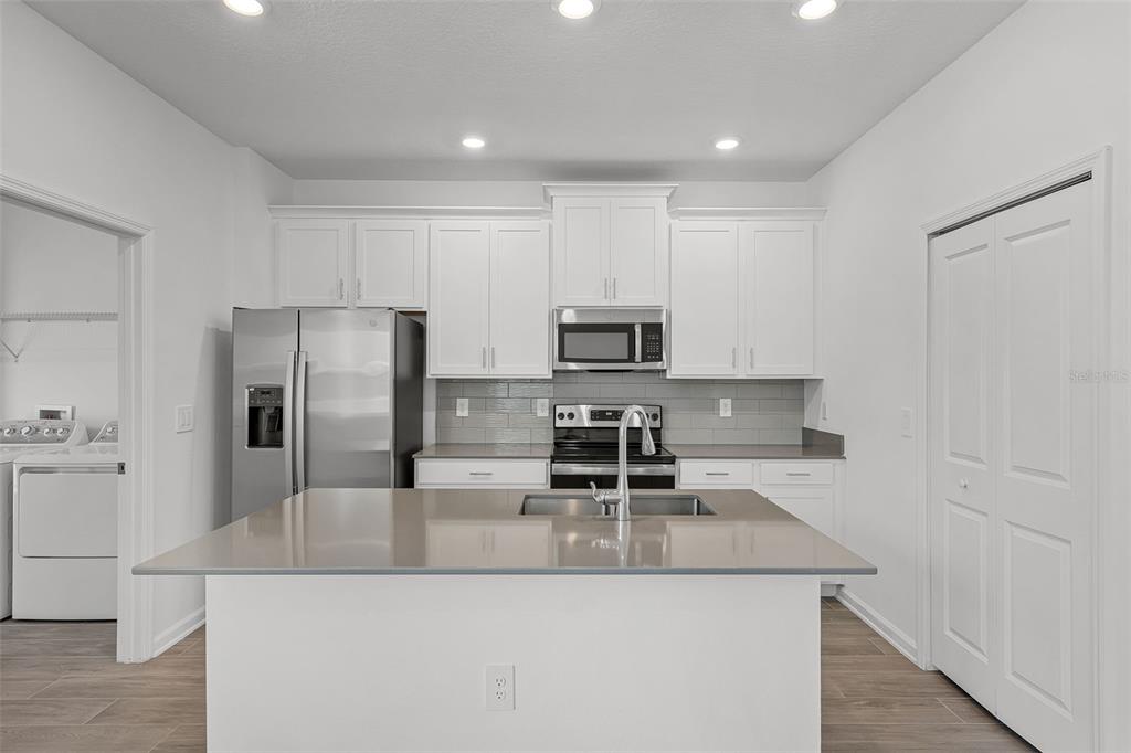 A modern kitchen features white cabinets, stainless steel appliances, a gray island, and tile backsplash — 2563 RELAXING LANE, KISSIMMEE, FL