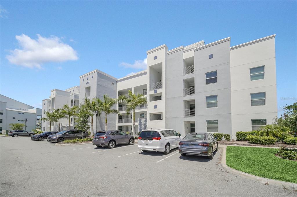 A multi-story apartment building with a parking lot in the foreground under a blue sky — 4721 CLOCK TOWER DRIVE UNIT 304, KISSIMMEE, FL