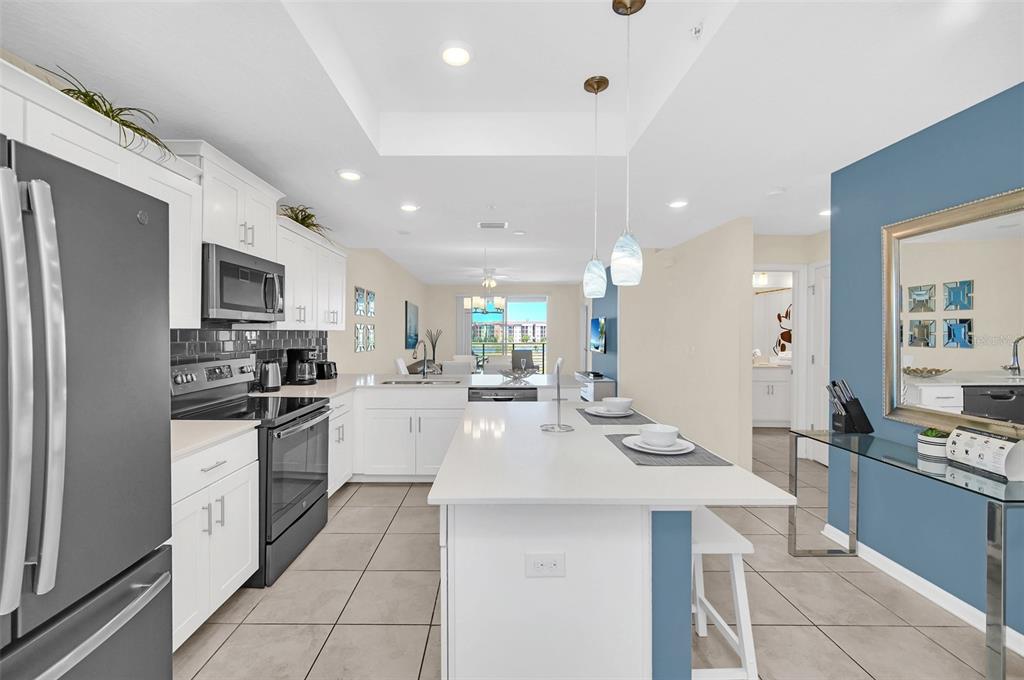 A modern kitchen features white cabinetry, stainless steel appliances, a center island, and tile flooring — 4721 CLOCK TOWER DRIVE UNIT 304, KISSIMMEE, FL