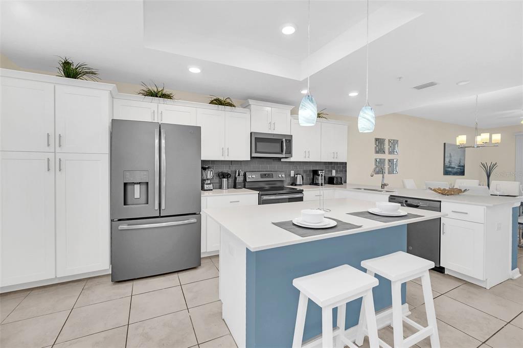 A modern kitchen features white cabinets, a blue island, stainless steel appliances, and tile flooring — 4721 CLOCK TOWER DRIVE UNIT 304, KISSIMMEE, FL