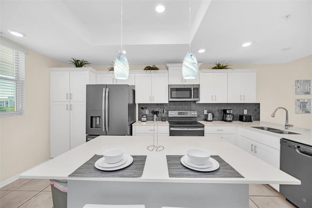 A modern kitchen features white cabinetry, stainless steel appliances, a gray tile backsplash, and an island — 4721 CLOCK TOWER DRIVE UNIT 304, KISSIMMEE, FL