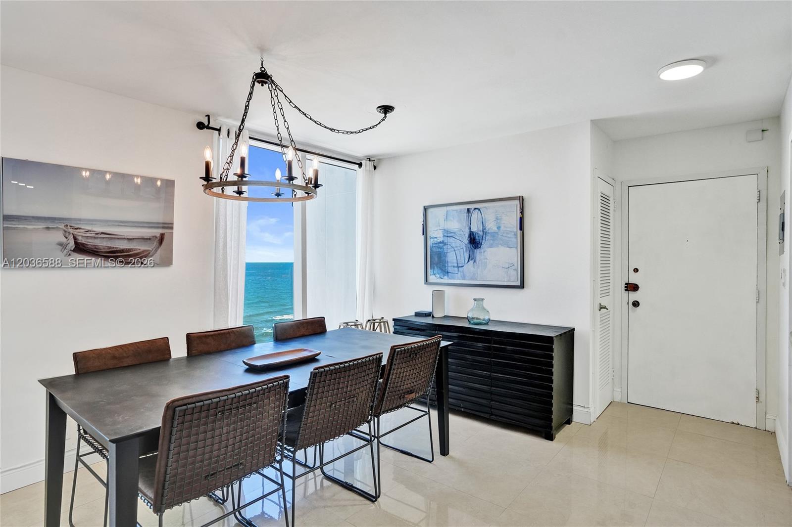 A dining room features a dark table, woven chairs, a chandelier, and an ocean view — 2030 S Ocean Dr # 821, Hallandale Beach FL 33009, HALLANDALE BEACH, FL