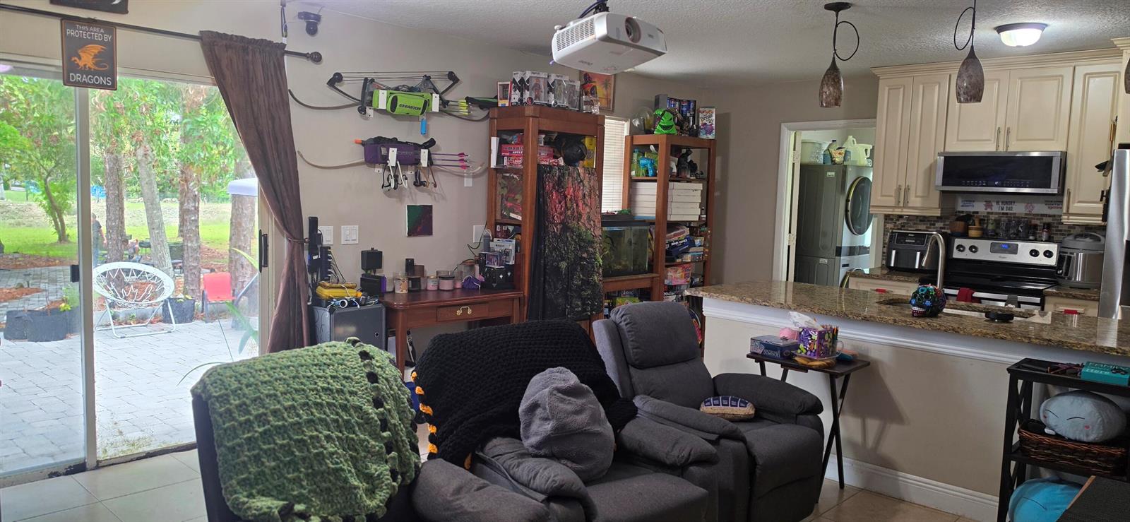 A living room with a projector, archery equipment, and an open kitchen with granite countertops — 15779 77th Place N, Loxahatchee FL 33470, LOXAHATCHEE, FL