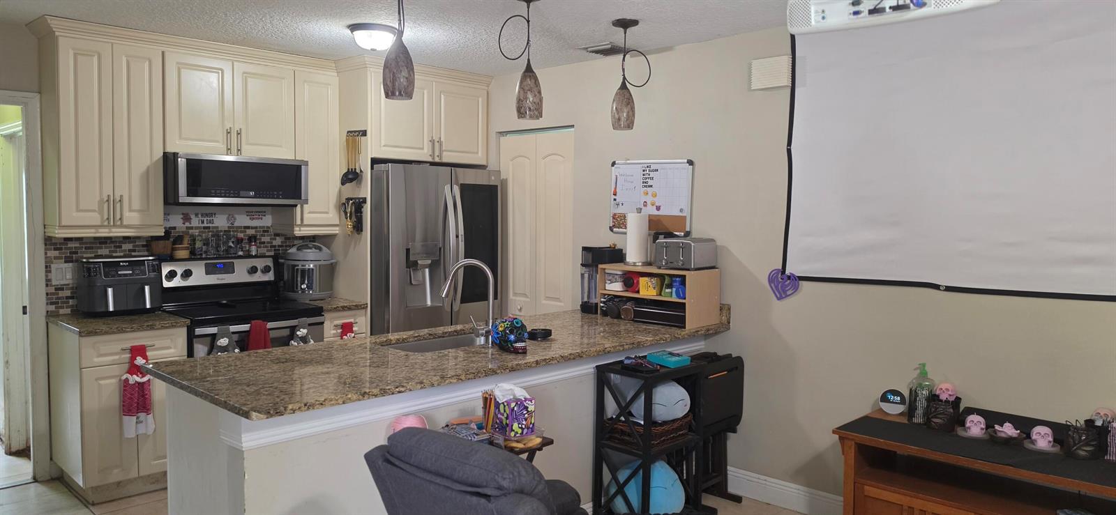 A kitchen with cream cabinets, granite countertops, stainless steel appliances, and a projector screen — 15779 77th Place N, Loxahatchee FL 33470, LOXAHATCHEE, FL