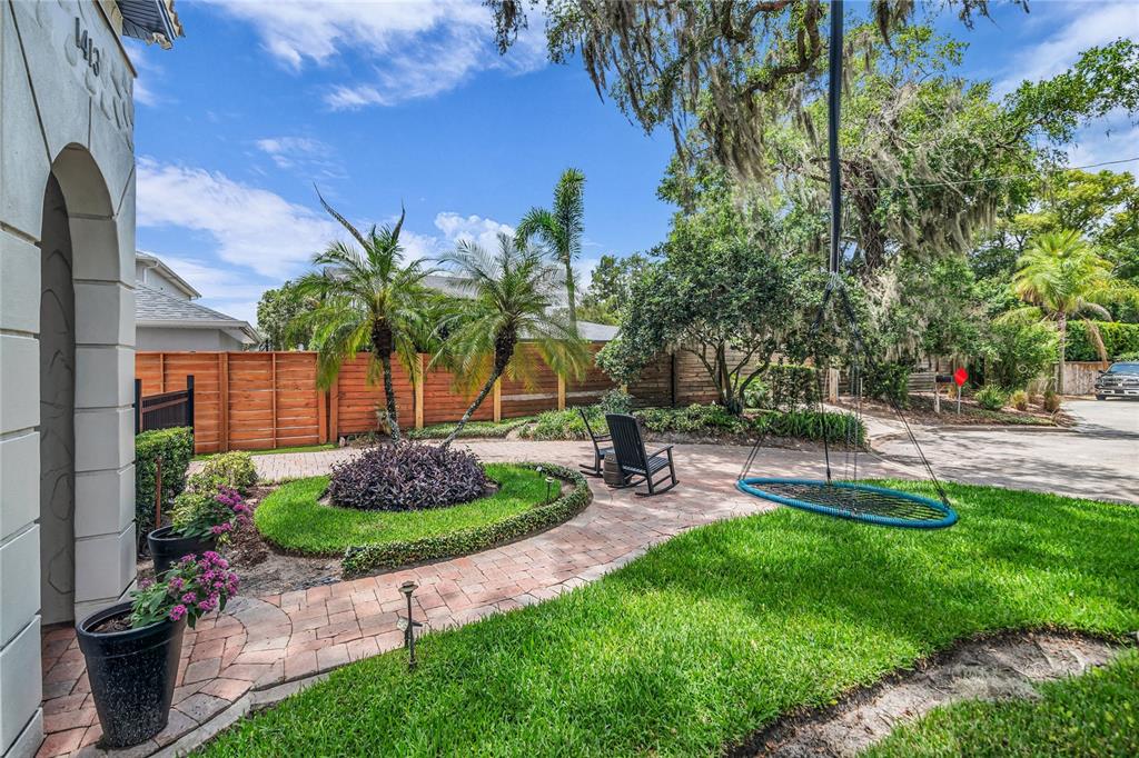 A brick walkway leads through a landscaped yard with palm trees and a hanging swing — 1413 OSCEOLA COURT, ORLANDO, FL