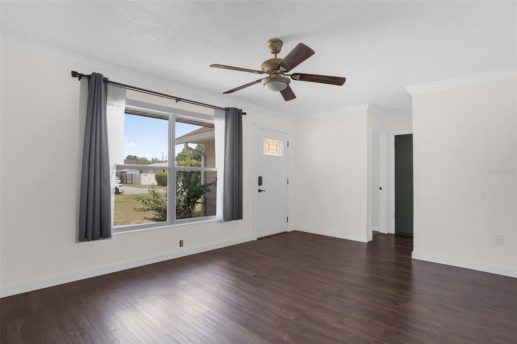An empty room features dark wood-look flooring, white walls, a ceiling fan, and a window — 706 JERSEY AVENUE, ST CLOUD, FL