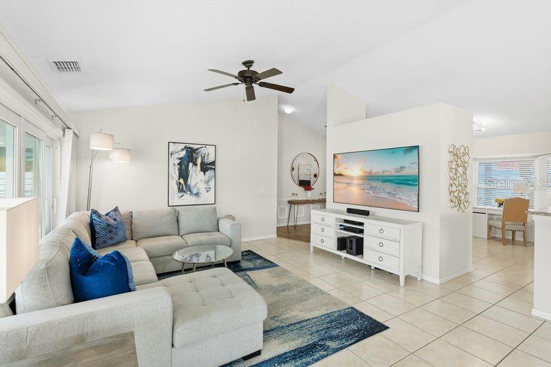 A living room features a sectional sofa, a television on a white console, and tile flooring — 4718 61ST AVENUE TERRACE W, BRADENTON, FL