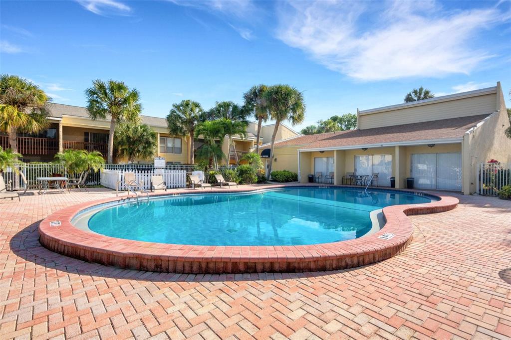 An outdoor swimming pool with a brick deck surrounded by palm trees and apartment buildings — 3413 CLARK ROAD UNIT 114, SARASOTA, FL