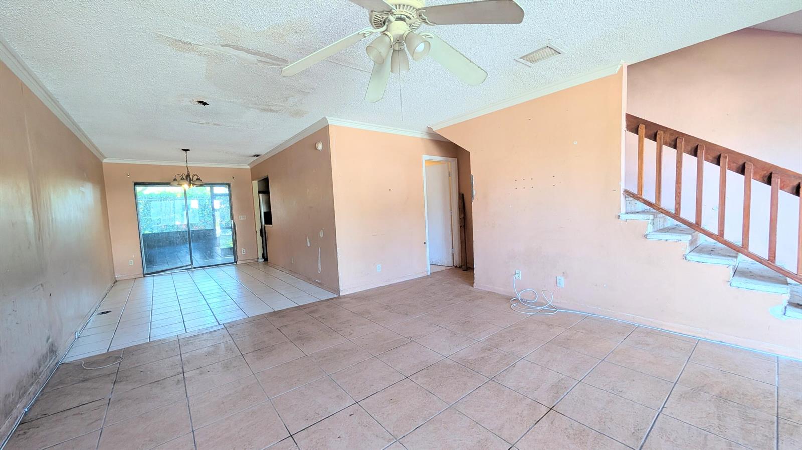 An empty living room features peach-colored walls, tiled floors, a ceiling fan, and a wooden staircase — 807 Riverside Drive # 7, FL 33463, FL
