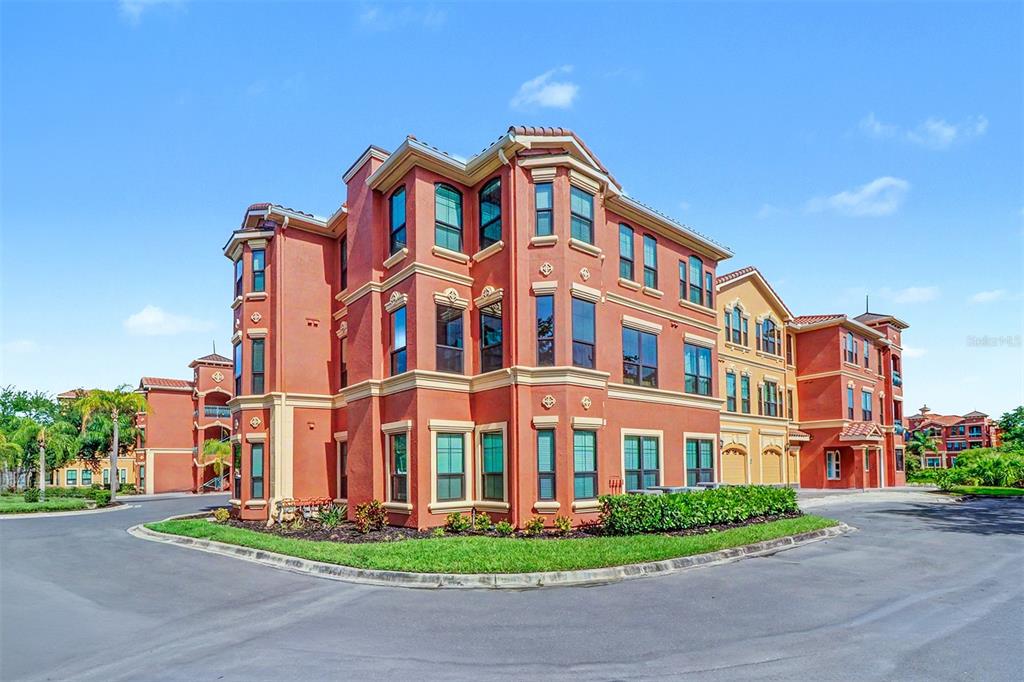 A multi-story, terracotta-colored apartment building stands under a clear blue sky — 2746 VIA TIVOLI UNIT 110B, CLEARWATER, FL