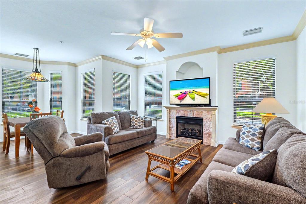A living room with a fireplace, television, ceiling fan, and brown furniture on wood floors — 2746 VIA TIVOLI UNIT 110B, CLEARWATER, FL