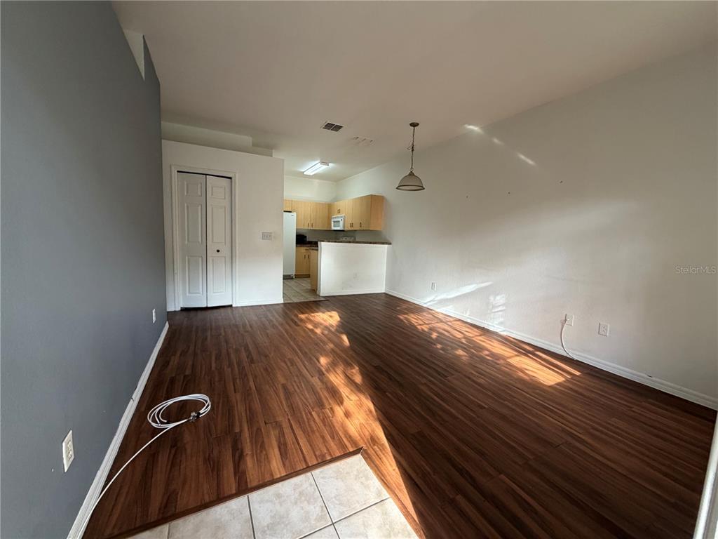 An open-concept living area features wood-look flooring, a gray accent wall, and an adjacent kitchen — 353 PORT PLEASANT DRIVE UNIT 353, KISSIMMEE, FL