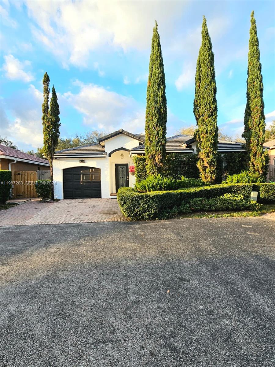 A single-story house with a black garage door and three tall cypress trees in front — 8003 SW 158th Pl, Miami FL 33193, MIAMI, FL