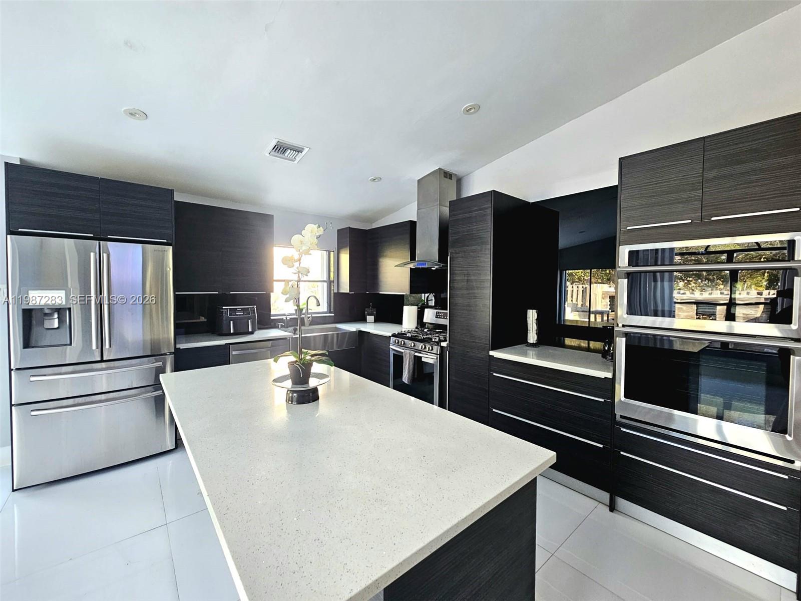 A modern kitchen features dark wood cabinetry, a large white island, and stainless steel appliances — 8003 SW 158th Pl, Miami FL 33193, MIAMI, FL