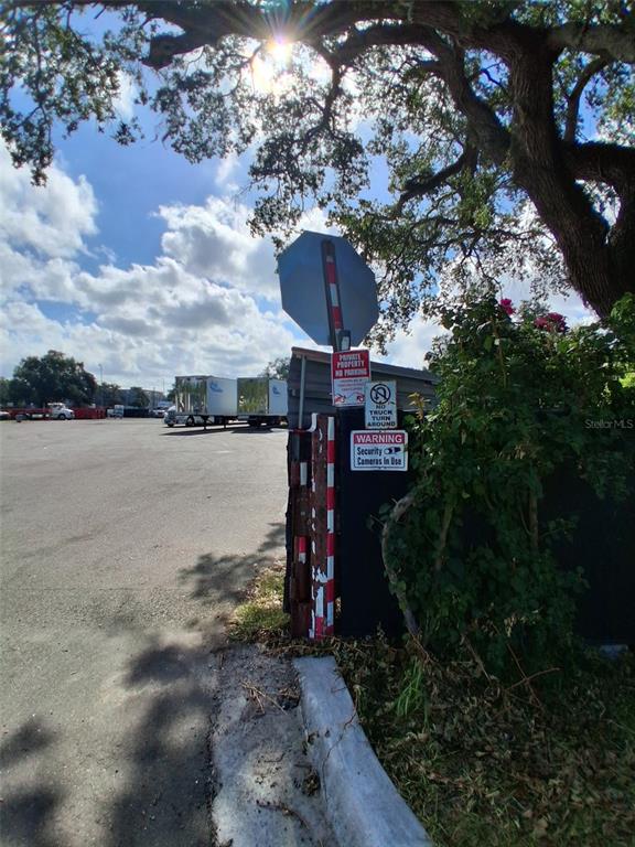A paved parking lot with semi-truck trailers is visible behind a signpost and a tree — 7001 CAUSEWAY BOULEVARD, TAMPA, FL