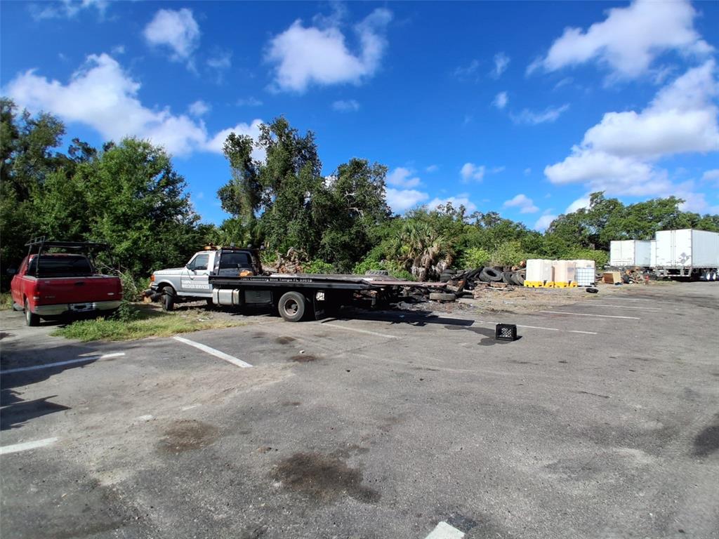 A flatbed tow truck is parked in a paved lot near a red pickup truck — 7001 CAUSEWAY BOULEVARD, TAMPA, FL