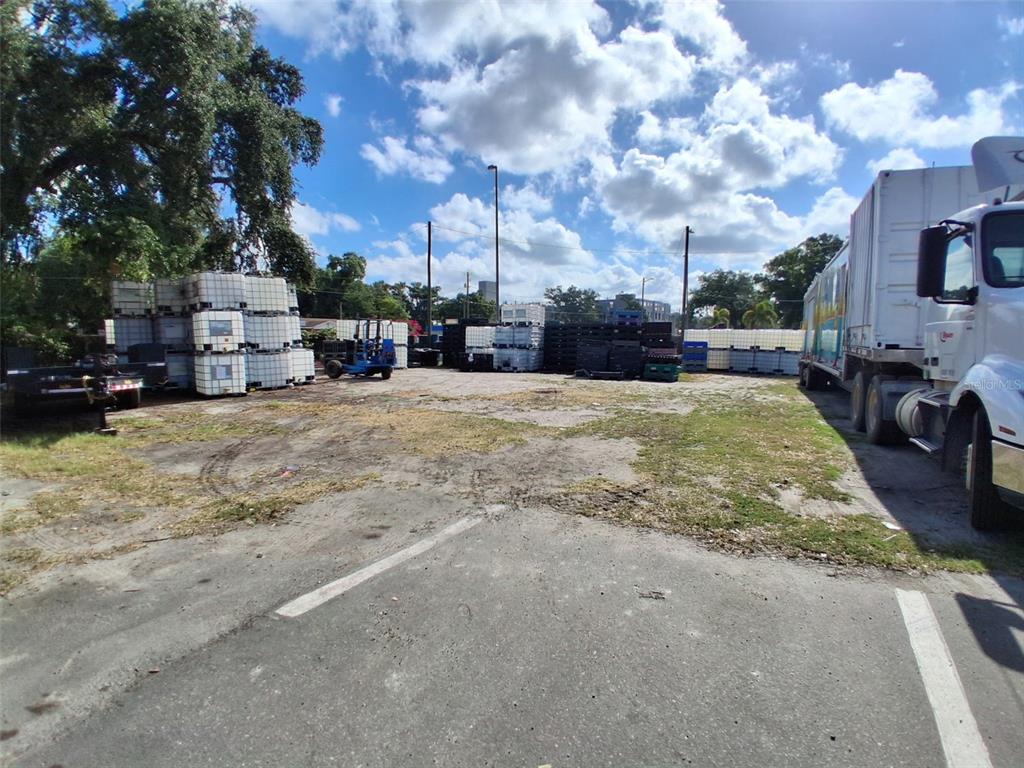An outdoor industrial storage lot features stacked shipping containers, a forklift, and a parked semi-truck — 7001 CAUSEWAY BOULEVARD, TAMPA, FL