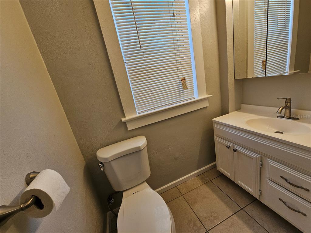 A bathroom features a white vanity, a toilet, and a window with horizontal blinds — 1408 N FORT HARRISON AVENUE UNIT B, CLEARWATER, FL
