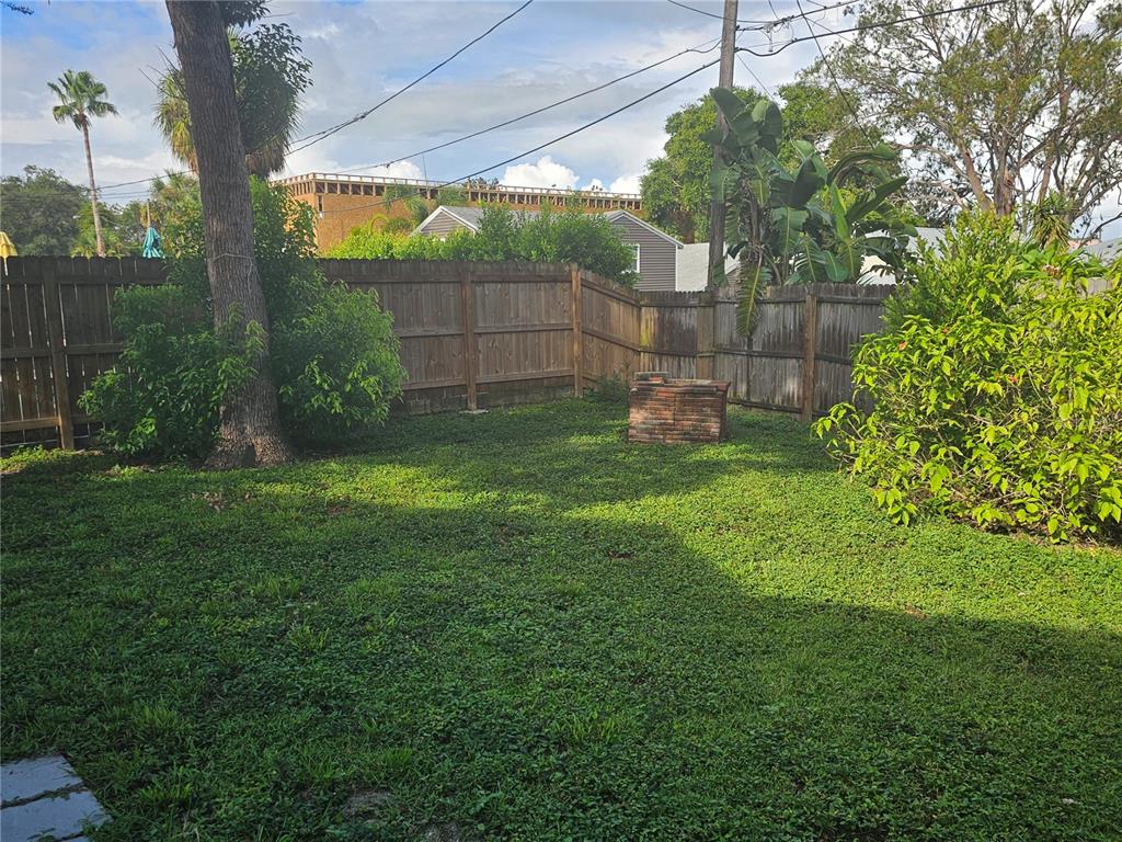 A grassy backyard features a wooden fence, a large tree, and a brick fire pit — 1408 N FORT HARRISON AVENUE UNIT B, CLEARWATER, FL