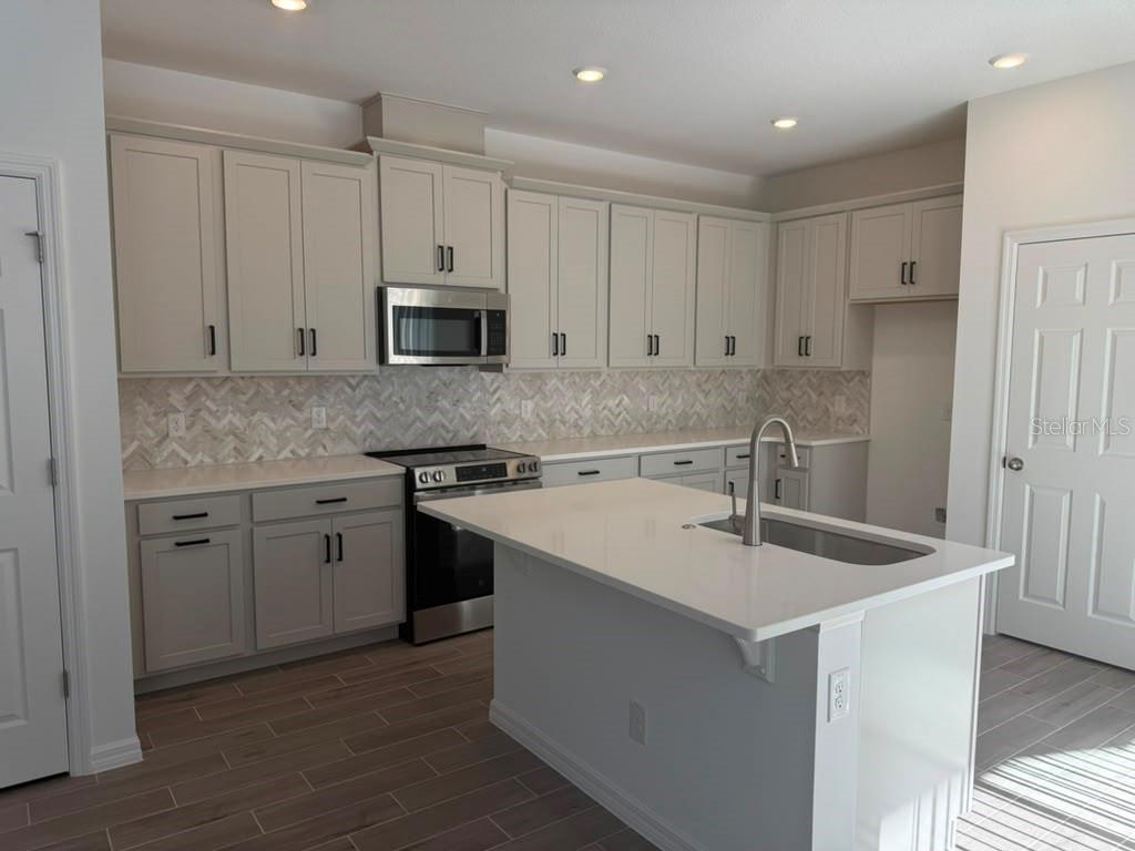 A kitchen with light gray cabinets, white countertops, a center island, and herringbone tile backsplash — 482 WINSOME ALLEY, GROVELAND, FL