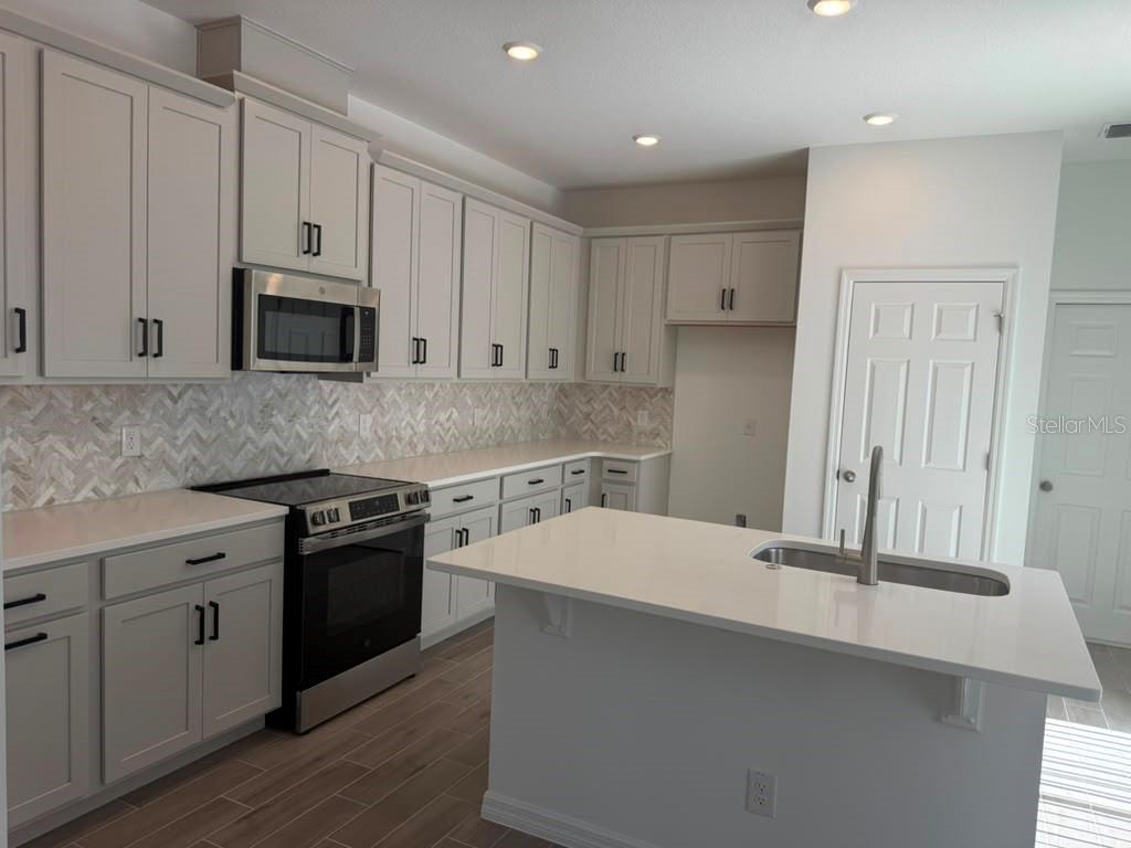 A kitchen with light gray cabinets, white countertops, stainless steel appliances, and a center island — 482 WINSOME ALLEY, GROVELAND, FL