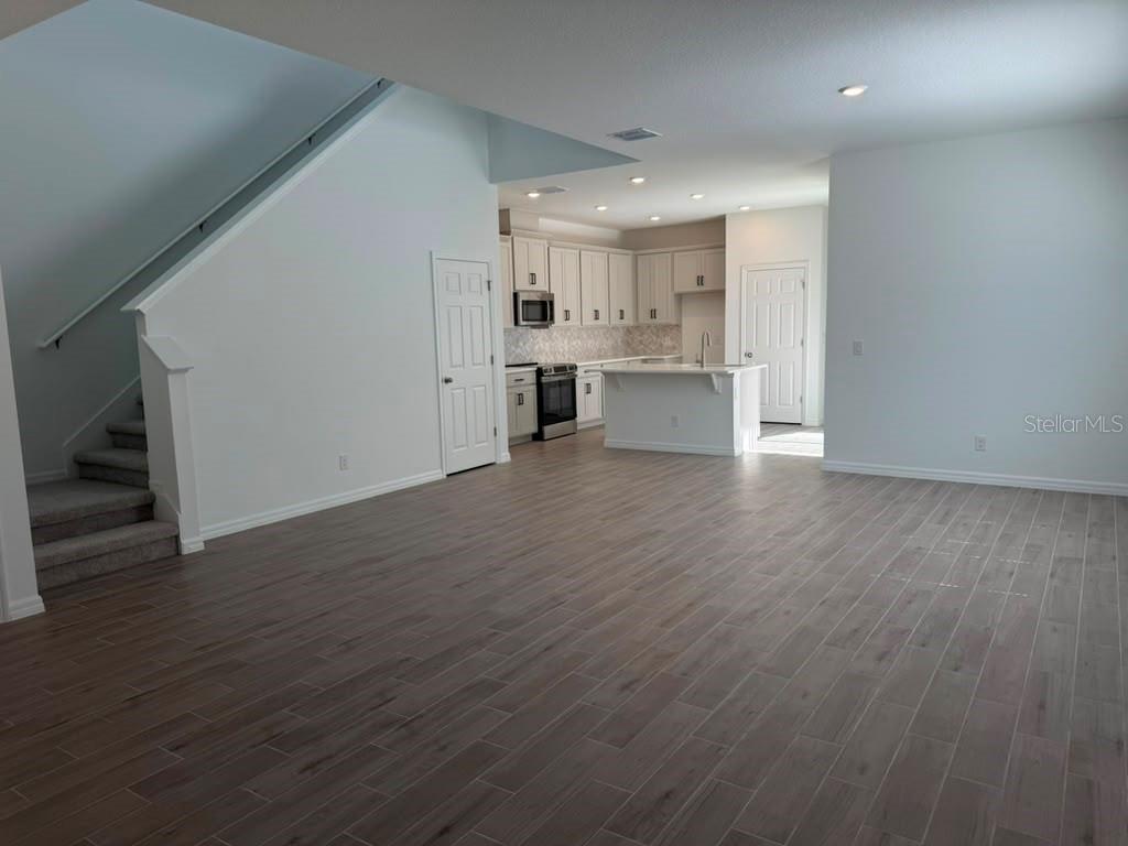 An open-concept living area features wood-look tile flooring, a staircase, and a white kitchen — 482 WINSOME ALLEY, GROVELAND, FL