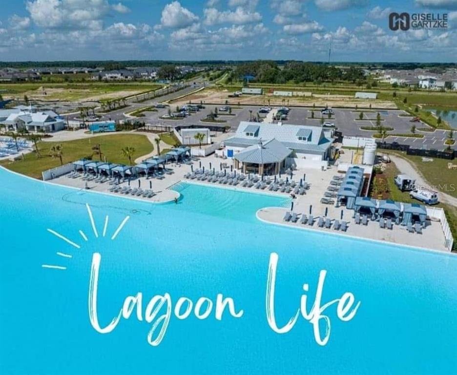An aerial view shows a large swimming lagoon with surrounding lounge chairs and a clubhouse — 11367 CAY SPRUCE WAY, SAN ANTONIO, FL