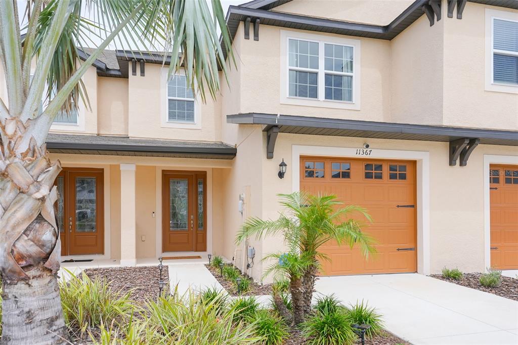 A two-story townhouse exterior features tan stucco walls, a brown garage door, and palm trees — 11367 CAY SPRUCE WAY, SAN ANTONIO, FL