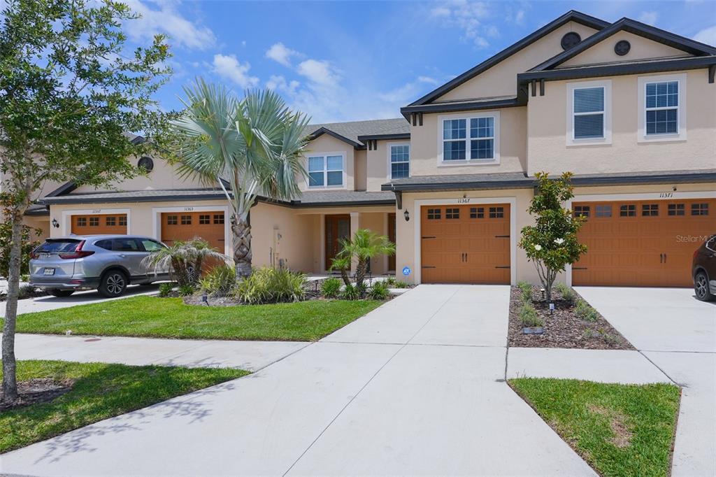 A multi-unit townhouse exterior features beige stucco walls, brown garage doors, and a concrete driveway — 11367 CAY SPRUCE WAY, SAN ANTONIO, FL