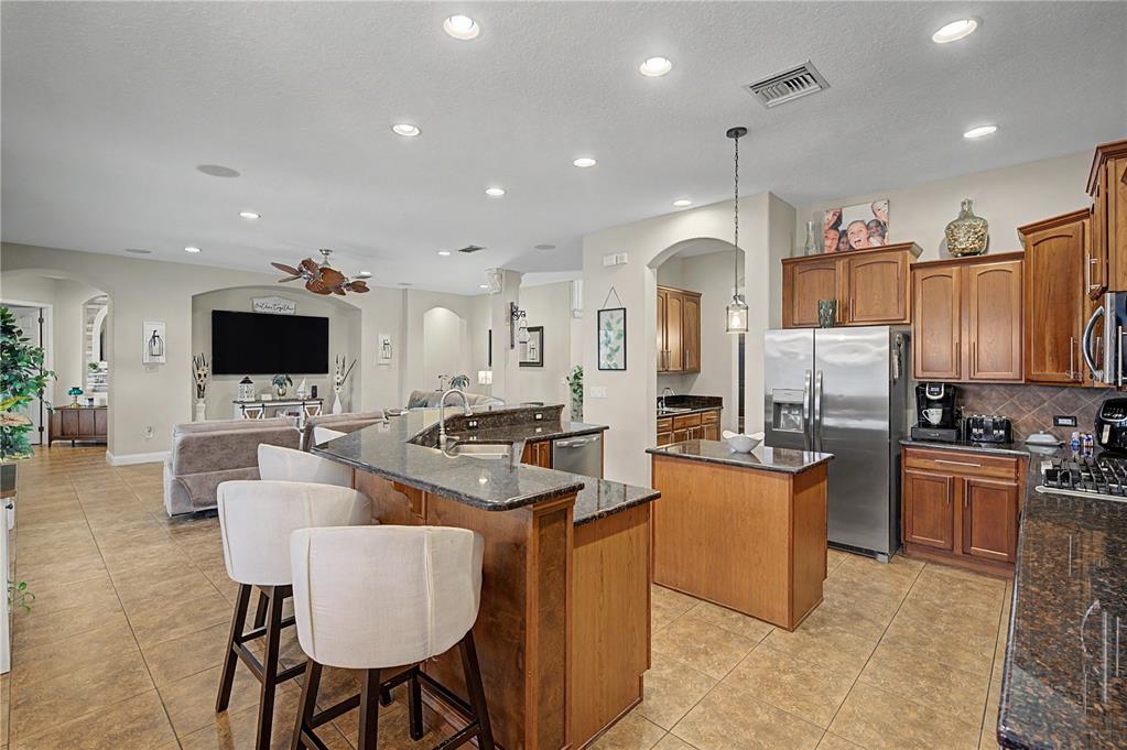 A kitchen with wood cabinets and granite countertops opens to a living area with tile floors — 3038 MARBLE CREST DRIVE, LAND O LAKES, FL
