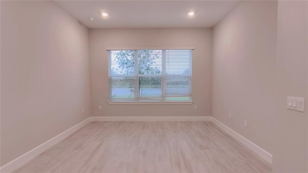 An empty room with light-colored wood flooring, neutral walls, and a large window with blinds — 5659 NEVIS TERRACE, KISSIMMEE, FL