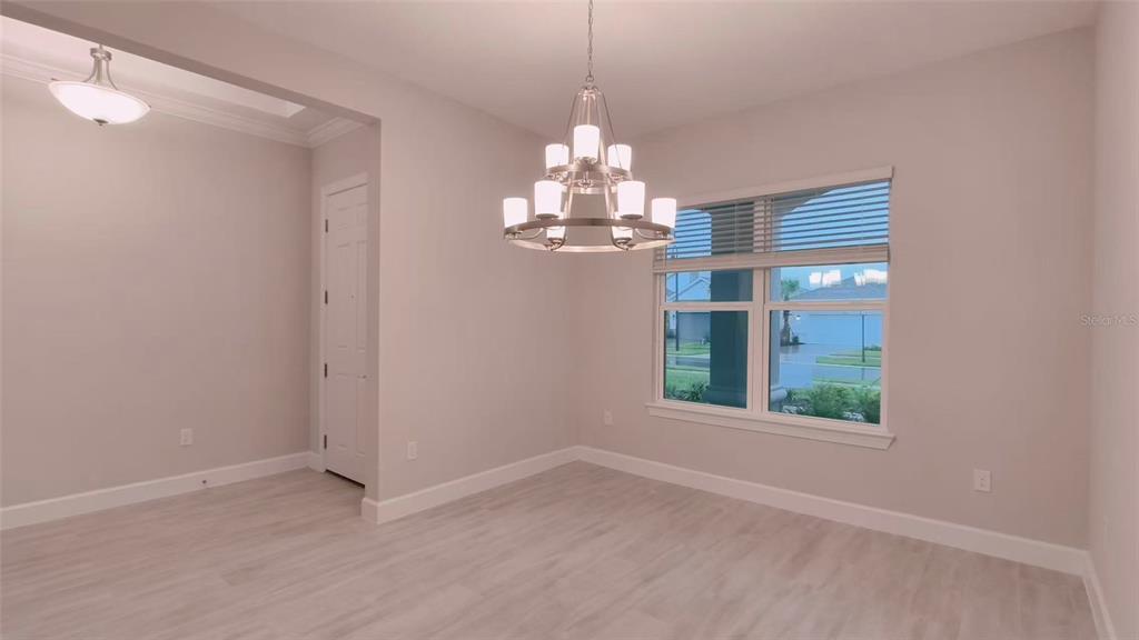 A dining room with light wood-look flooring, a modern chandelier, and a large window — 5659 NEVIS TERRACE, KISSIMMEE, FL