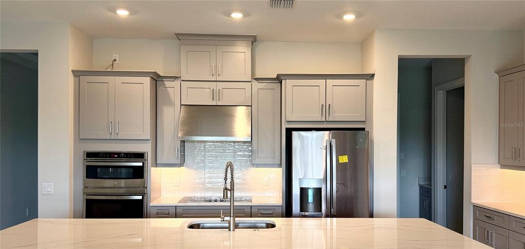 A modern kitchen features gray cabinetry, stainless steel appliances, and a large white island — 5659 NEVIS TERRACE, KISSIMMEE, FL