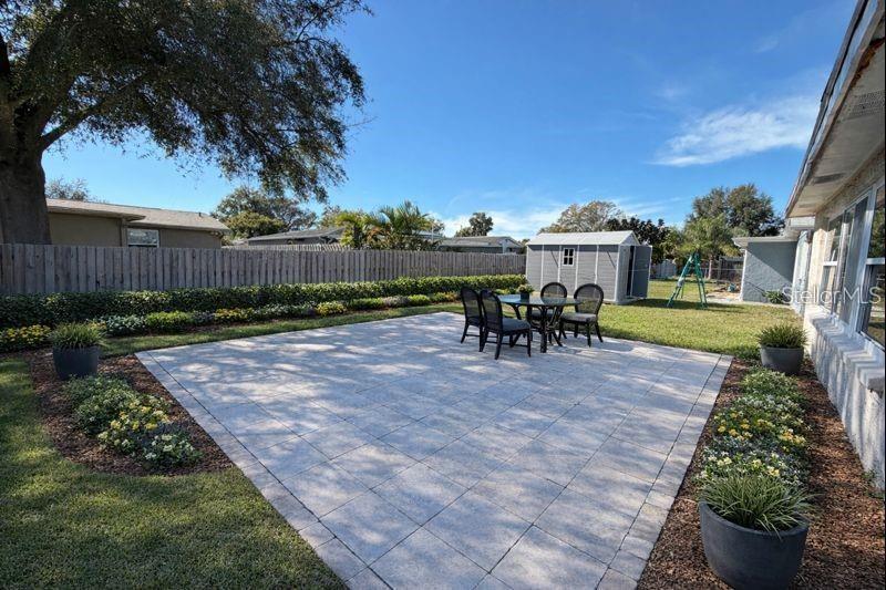 A paved patio with outdoor furniture sits in a backyard next to a storage shed — 3118 ELKRIDGE DRIVE, HOLIDAY, FL