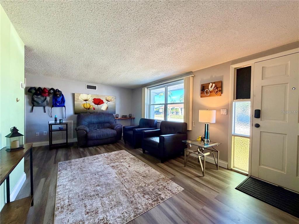 A living room features wood-look flooring, a textured ceiling, a rug, and seating furniture — 3118 ELKRIDGE DRIVE, HOLIDAY, FL