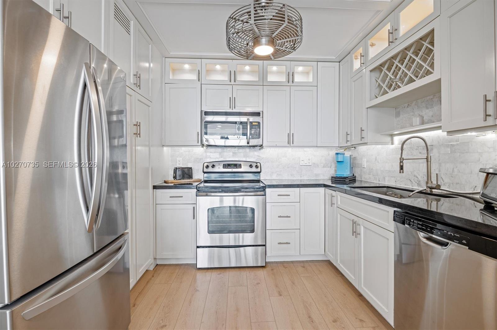 A kitchen features white cabinets, stainless steel appliances, black countertops, and light wood flooring — 3505 S OCEAN DR # 607, Hollywood FL 33019, HOLLYWOOD, FL