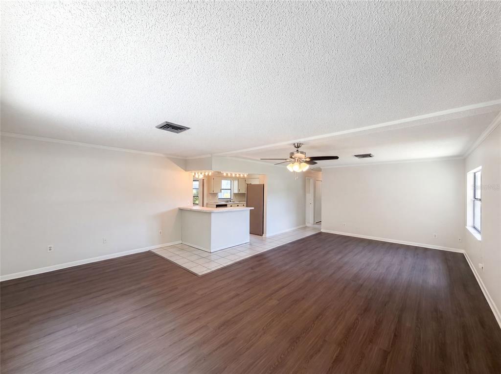 A spacious living room with wood-look flooring, a ceiling fan, and an open kitchen area — 3129 AVENUE W NW, WINTER HAVEN, FL