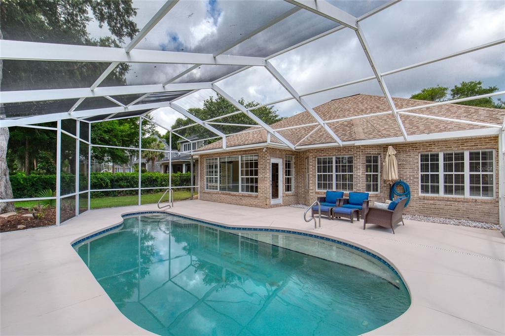 A swimming pool with a screened enclosure sits on a patio behind a brick house — 5 WATERCLIFF LANE, ORMOND BEACH, FL