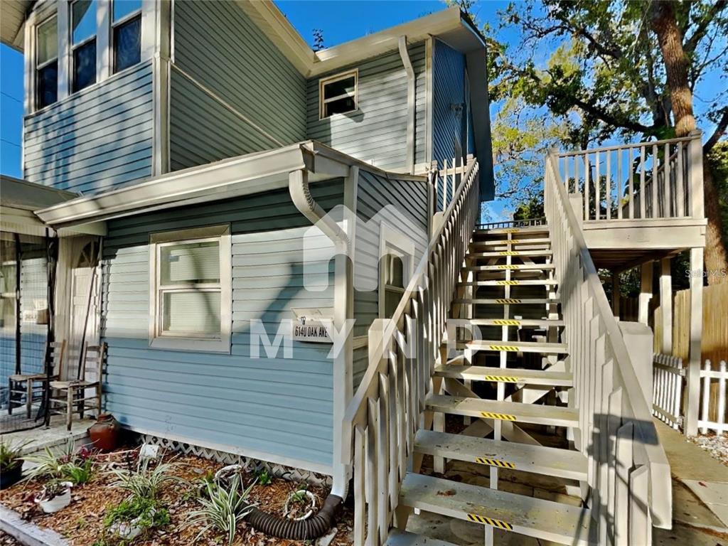 A blue-sided house features an exterior wooden staircase leading to an upper-level deck — 614 OAK AVENUE, CLEARWATER, FL