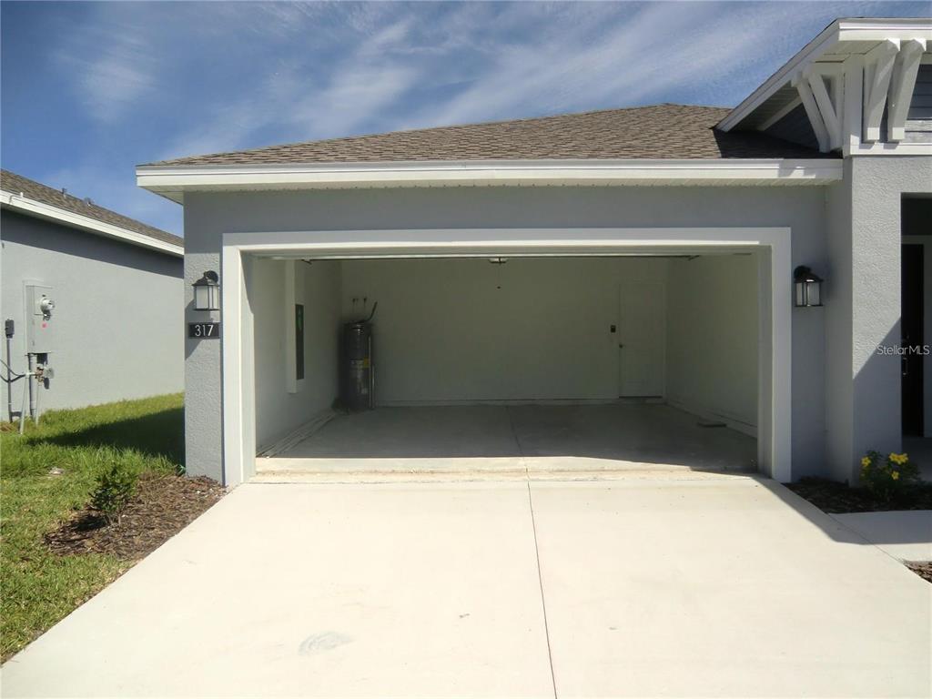 An open two-car garage with a concrete floor and a water heater inside — 317 LOCH COURT, DAVENPORT, FL