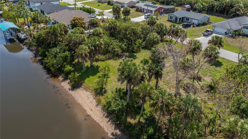 An aerial view shows a vacant, tree-covered waterfront lot situated between two residential houses — 18546 ASHCROFT CIRCLE, PORT CHARLOTTE, FL